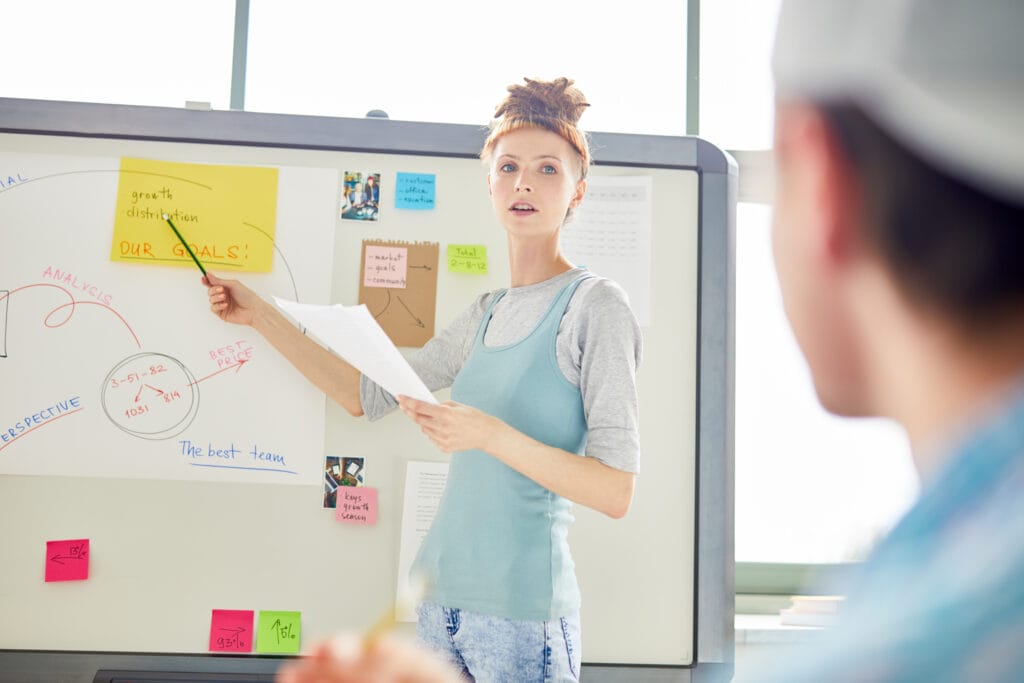 Company meeting where the presenter is pointing to goals on a whiteboard.