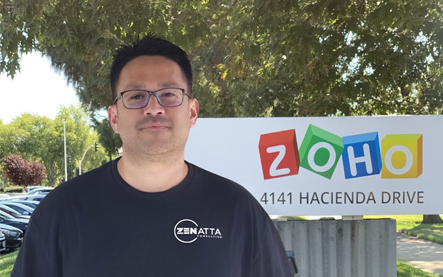 Freddy Hernandez, Sr. Producer at Zenatta Consulting standing in front of a Zoho Sign under a tree on a bright sunny day