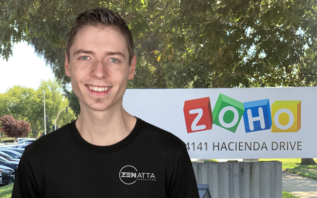 Colton Weidner, Developer at Zenatta Consulting standing in front of a big Zoho sign